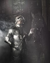 Knight wearing armour standing beside his horse in the woods