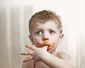 Toddler licking tomato sauce off his thumb