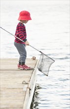 Child standing on dock by the sea with fishing net in hand