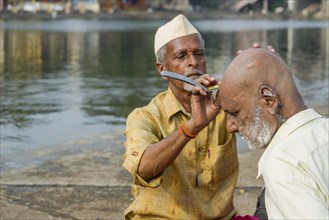 A barber is shaving a pilgrim at the banks of the holy river Godwari