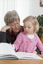 Grandmother reading from a book to her granddaughter