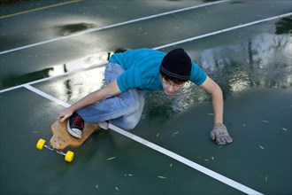 Teenage boy skating with his longboard in a tennis court yard