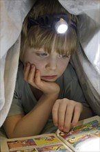 Boy reading a comic with a head lamp under the duvet