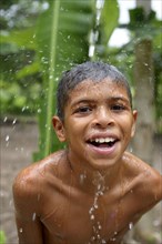 Brazilian boy holding his head in a stream of water and laughing