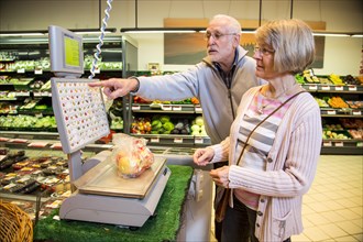 Senior couple weighing fruit at the self-service scales while shopping in the fruit and vegetables department of a supermarket