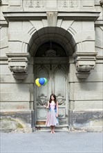 Girl holding balloons in front of an old door