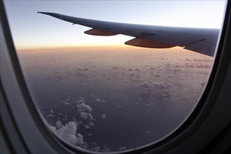 Wing of a high flying Boeing 777 long reach aircraft seen through passenger window at sunset