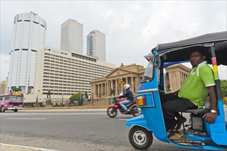 Tuk tuk driver with the building of the Bank of Ceylon at the back