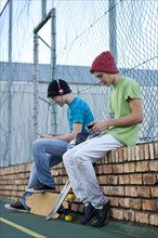 Two teenage boys sitting on a brick wall