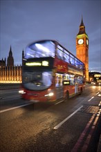 Red double-decker bus in front of Elizabeth Tower or Big Ben and the Palace of Westminster or Houses of Parliament at dusk