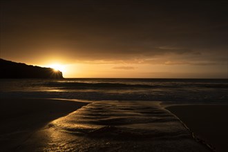 A brook flows over the sandy beach into the sea