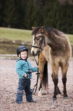 Young child wearing a riding helmet holding a pony