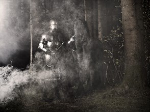 Knight wearing armour standing beside his horse in the woods