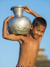 Smiling boy carrying water in a water container made of aluminium
