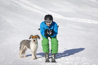 A skier and his dog with snow goggles on a ski slope