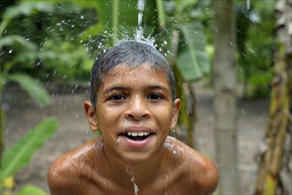 Brazilian boy holding his head in a stream of water and laughing