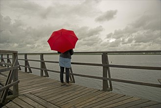Woman holding a red umbrella on a wharf on Federsee lake