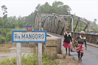Two women crossing an old iron bridge over the Mangoro River