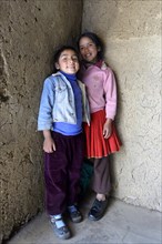 Two girls standing inside a mud-walled hut