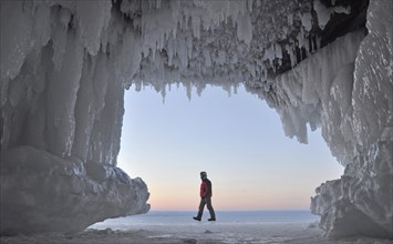 Ice formations and icicles hanging from ceiling in a cave and a man walking on frozen Lake Superior