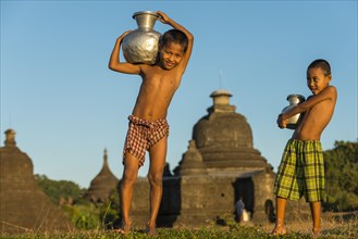 Smiling boys carrying water in front of a pagoda or a temple