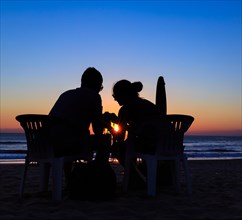 A couple sitting on the beach at sunset
