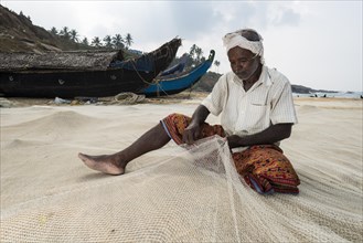Fisherman repairing fishing nets on the beach