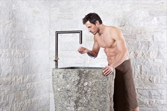 Bare-chested man standing at a water fountain in a spa complex