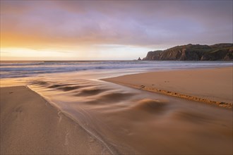 A brook flows over the sandy beach into the sea