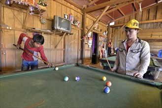 Two Cambodian youths playing pool billiards in a simple wooden hut