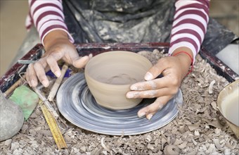 Hands molding a piece of pottery on a wheel head