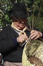 Elderly man in traditional costume making a basket at a traditional handicraft fair