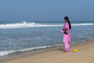 Woman wearing a pink shalwar kameez standing on the beach facing the sea