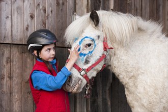 Girl wearing a riding helmet painting a pony with finger paints