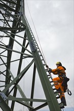 Overhead transmission cable installer climbing a mast to install insulated cable on a newly built high-voltage transmission mast