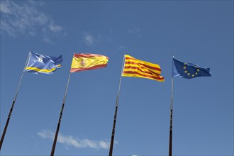 Flags of Spanish regions on flagpoles against blue sky
