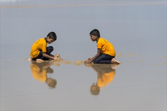 Two schoolboys wearing yellow shirts playing on the beach