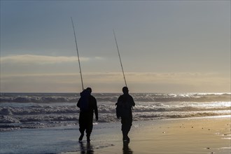 Two anglers walking with their fishing rods along the seaside beach