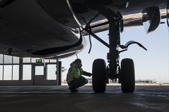 Worker kneeling next to at the undercarriage of an aircraft