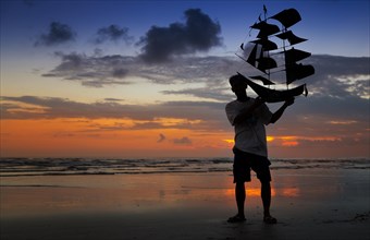 Silhouette of a man holding a kite shaped like a ship