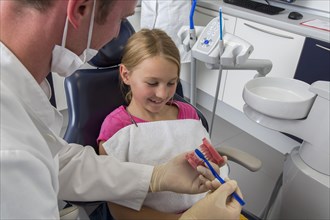 Dentist showing a girl the proper use of a toothbrush