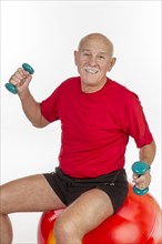 Elderly man sitting on a stability ball holding small dumbbells