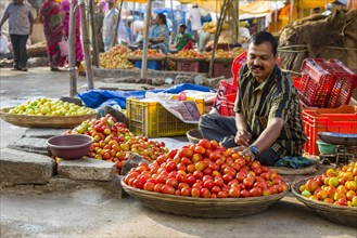 A man is selling tomatoes at the weekly vegetable market