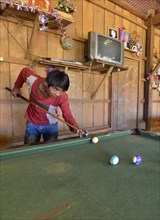 Cambodian youth playing pool billiards in a simple wooden hut