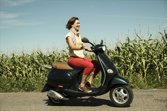 A smiling woman driving with her scooter through fields