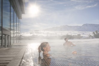 Woman and man sitting in a heated swimming pool in winter with steaming water
