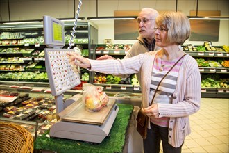 Senior couple weighing fruit at the self-service scales while shopping in the fruit and vegetables department of a supermarket