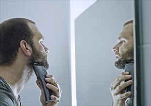 Man shaving his beard in front of a mirror
