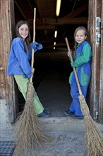 Two sisters holding stable brooms