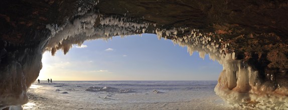 Ice formations and icicles hanging from ceiling in a cave and people walking on frozen Lake Superior